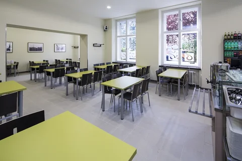 Jídelna s limetkovými stoly a černými židlemi u vysokých oken
